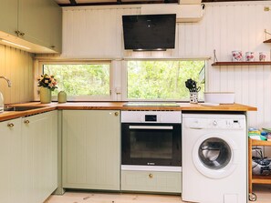 A compact kitchen with a Bosch dishwasher, oven, and washing machine, a window with a view of greenery, and a shelf with kitchen utensils. - 4 Person Holiday Home in Skibby (Skibby)