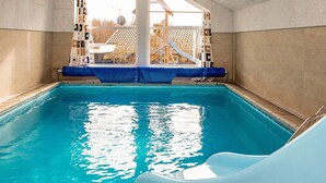 An indoor swimming pool with clear blue water, a slide, and a view of a house with a tiled roof. - 8 Person Holiday Home in Ebeltoft-by Traum (Ebeltoft)