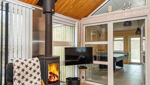 A cozy room with a wood-burning stove, a comfortable chair, a television, and a ping pong table. - 8 Person Holiday Home in Ebeltoft-by Traum (Ebeltoft)