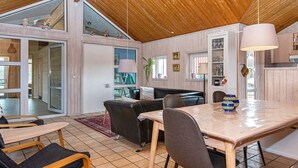 A spacious living area with a wooden ceiling, a black leather sofa, a dining table with chairs, and a kitchen area with wooden cabinets and a hanging light fixture. - 8 Person Holiday Home in Ebeltoft-by Traum (Ebeltoft)