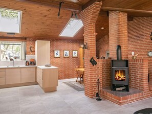 Eine moderne Küche mit Kamin aus Ziegeln, Holzbalkendecke und einem großen Fenster.