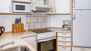 Une cuisine de taille réduite, dotée de meubles blancs, d’un four à micro-ondes, d’une cuisinière, d’un réfrigérateur et d’une machine à café.