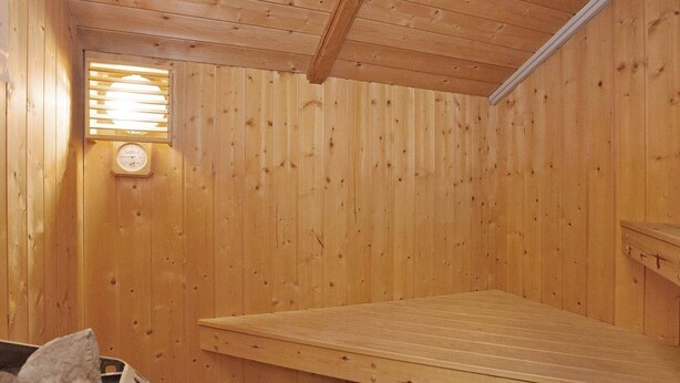 Un sauna en bois, équipé d’un banc, d’un thermomètre fixé au mur et d’une fenêtre avec des stores.