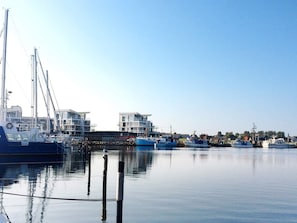 A marina with boats docked, a clear sky, and buildings in the background.