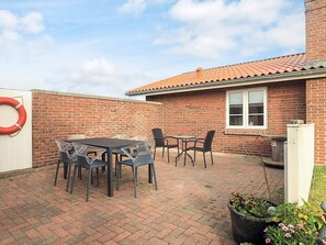 A brick building with a tiled roof, a patio with a table and chairs, and a life preserver on the wall.