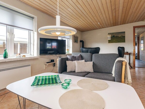 A living room with a flat-screen TV, a grey sofa, a white coffee table, and a wooden ceiling.