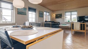 Un vaste espace de vie doté d’un plafond en bois, d’une table à manger avec des sets de table et d’un téléviseur en arrière-plan.