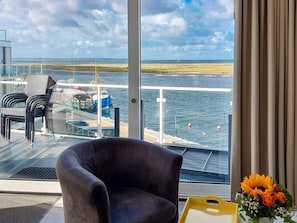 Una habitación con un ventanal grande que da a un muelle y al agua, una silla y una bandeja amarilla.