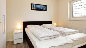 A bedroom with a bed, bedside tables, a nightstand, a window with a view, and a framed picture on the wall. - Holiday Home in GroÃŸenbrode (Grossenbrode)