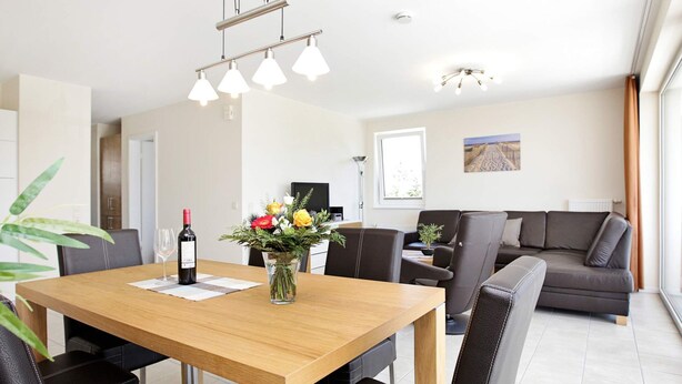 A modern living room with a wooden dining table, black leather chairs, a sofa, and a large window. - Holiday Home in GroÃŸenbrode (Grossenbrode)