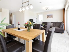 A modern living room with a wooden dining table, black leather chairs, a sofa, and a large window.