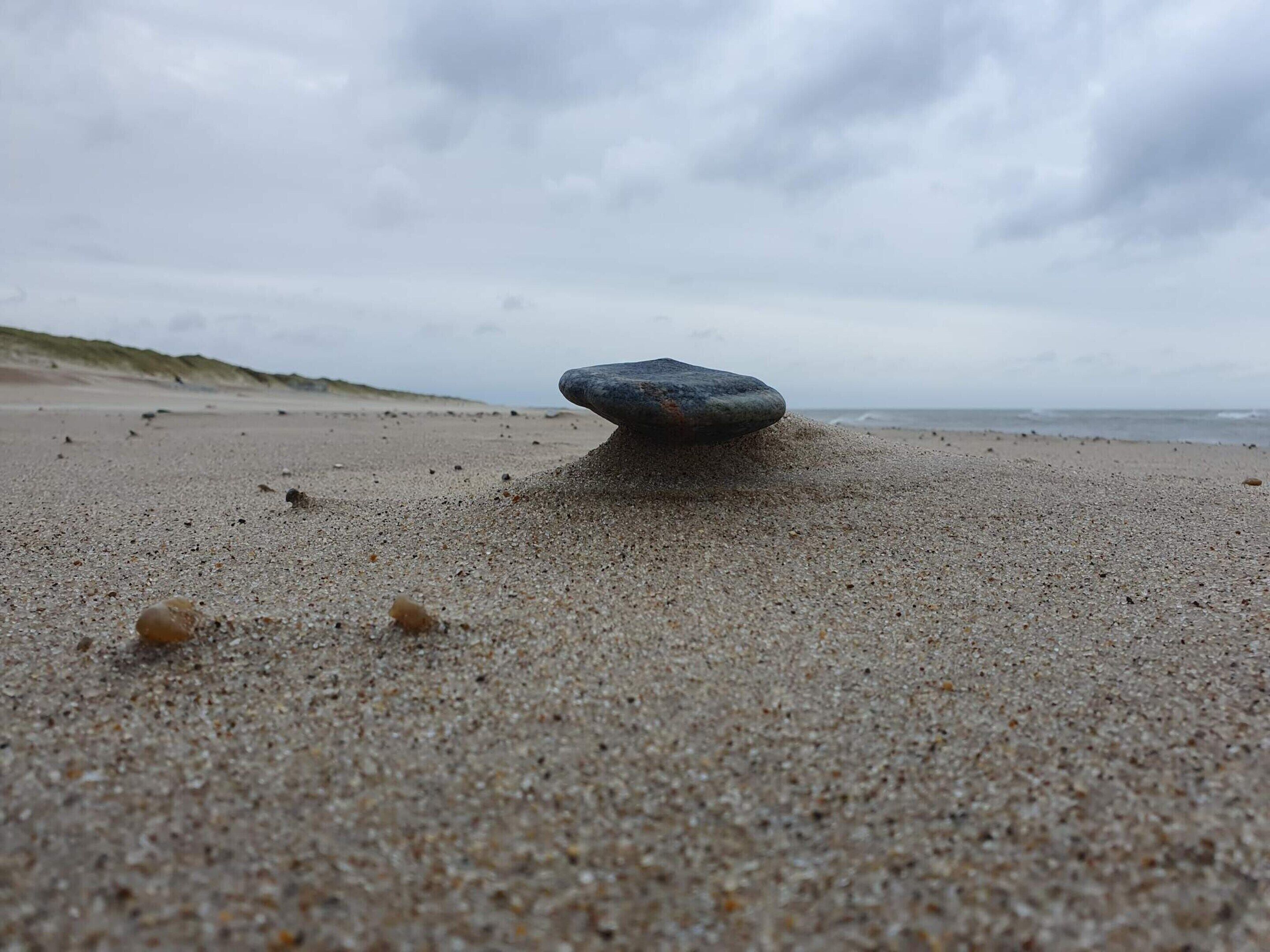 A pebble on a sandy beach with a cloudy sky in the background.