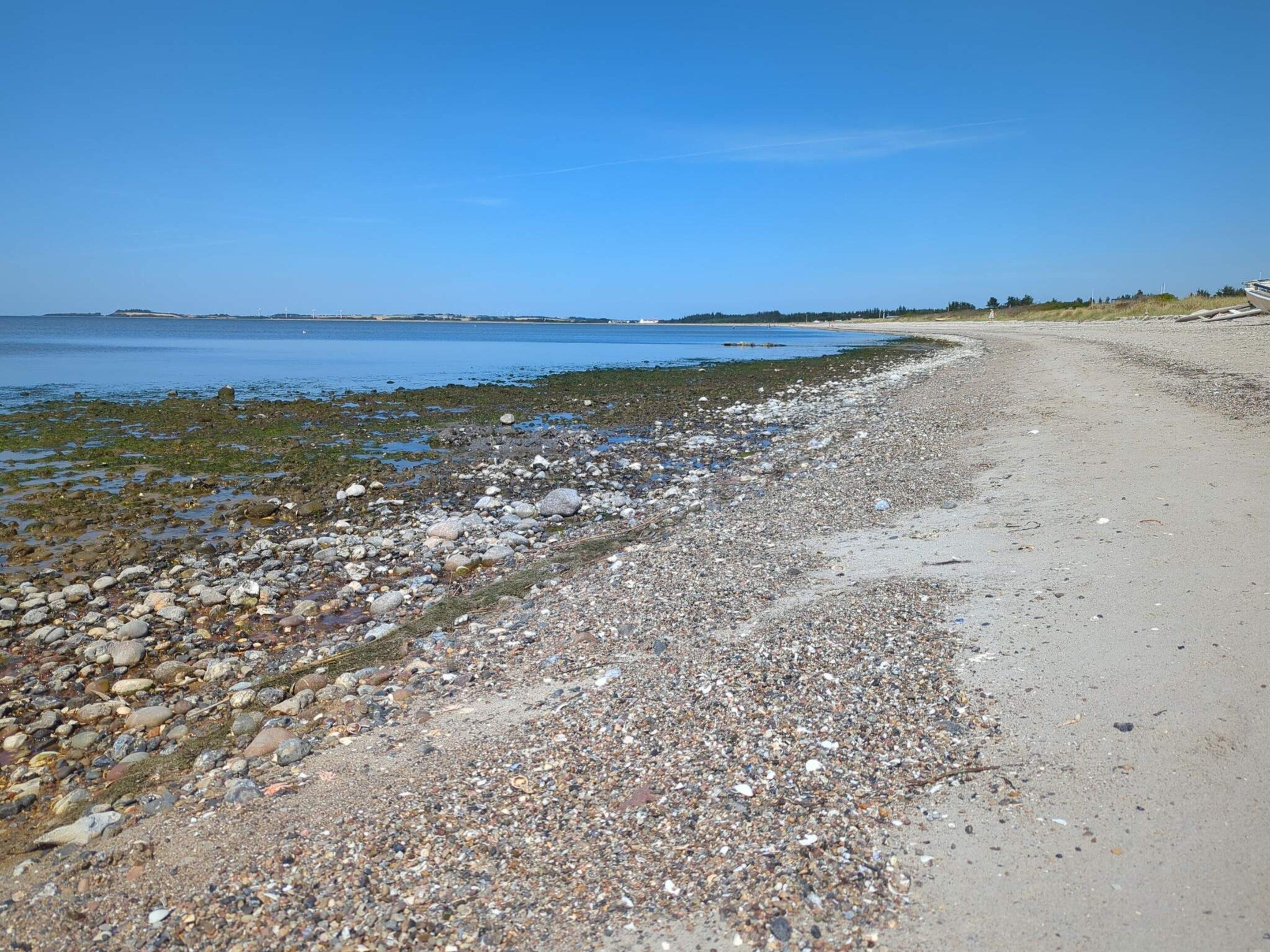 A pebbly beach with a clear sky and calm water.