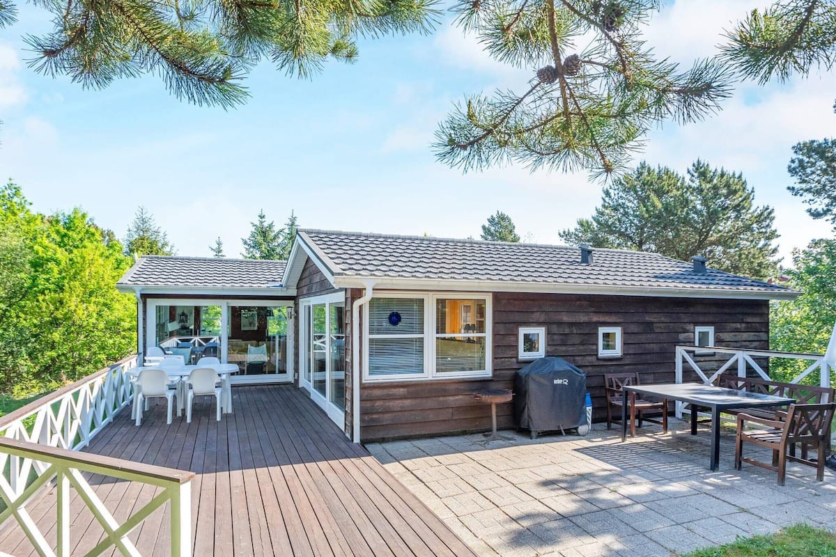A wooden cabin with a deck, outdoor seating, and a covered grill area.