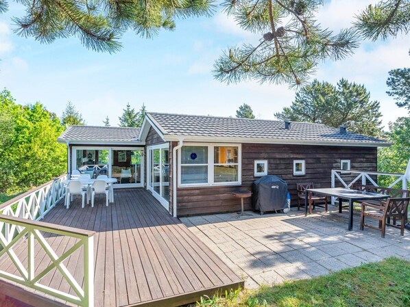 A wooden cabin with a deck, outdoor seating, and a covered grill area.