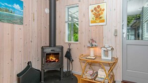 Ein gemütliches Zimmer mit Kamin, einem Korbstuhl, einem kleinen Tisch mit Lampe und einem gerahmten Bild an der Wand.