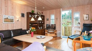 Ein gemütliches Wohnzimmer mit Holzboden, einer schwarzen Ledersofa, einem Couchtisch aus Holz und einem Fernseher auf einem Holzgestell.