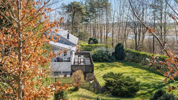 Ein modernes Haus mit einer Terrasse, umgeben von einem gepflegten Garten und Bäumen.