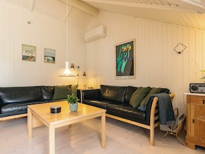 A living room with a black leather sofa, a wooden coffee table, and a radio on a wooden cabinet. - 6 Person Holiday Home in Humble (Sydlangeland)