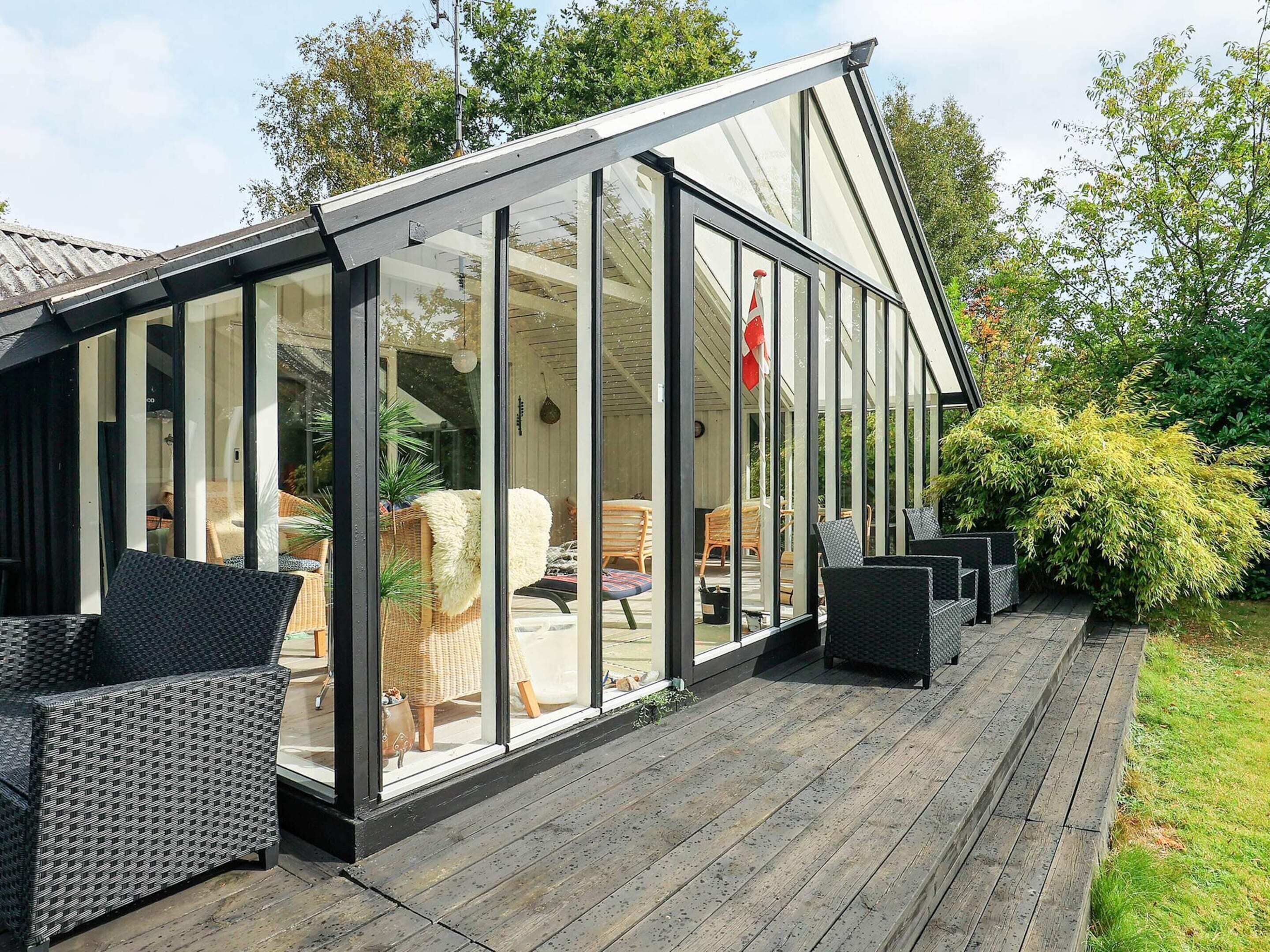 A covered patio area with glass walls, wicker furniture, and a wooden deck.