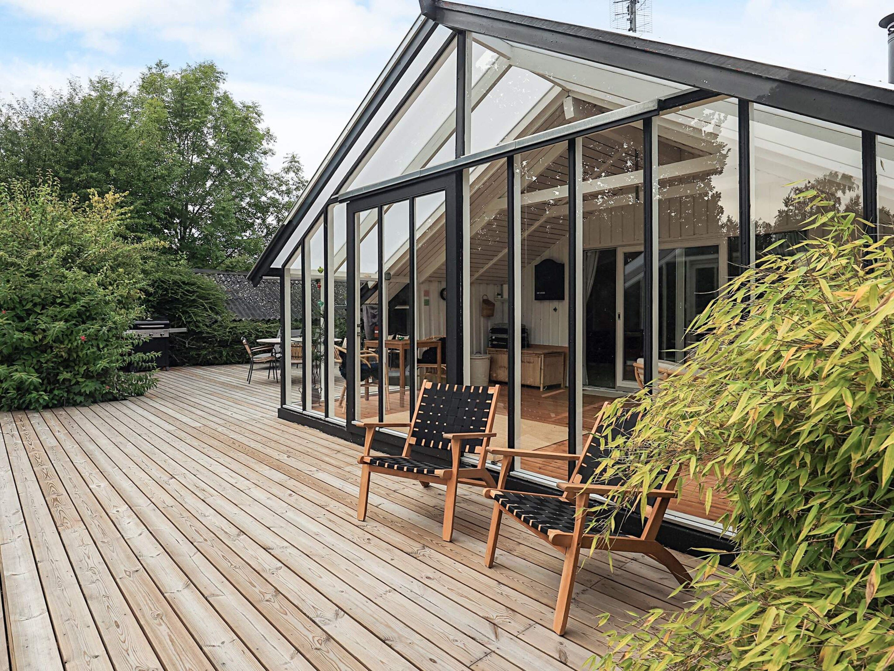 Une terrasse en bois avec deux chaises et une structure fermée par des parois de verre.