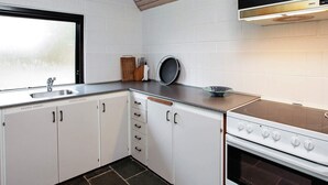 A compact kitchen with white cabinets, a stainless steel sink, a stove, and a window providing natural light. - Classic Holiday Home in Hals near Sea (Hals)