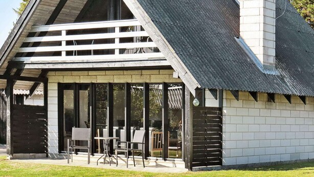 A modern building with a sloped roof, large windows, and a covered patio area with outdoor seating. - Classic Holiday Home in Hals near Sea (Hals)
