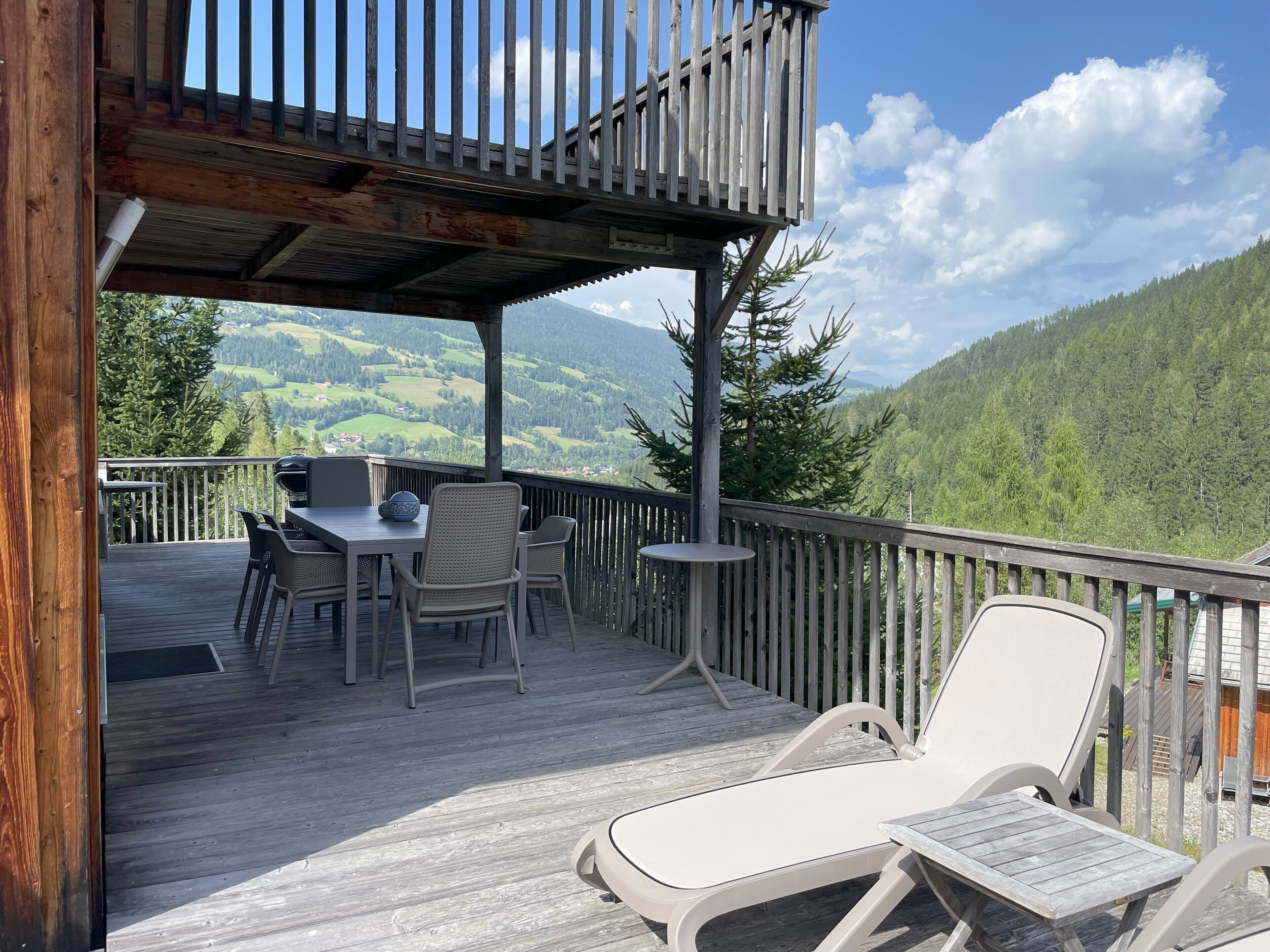 Une terrasse en bois, aménagée avec du mobilier d’extérieur, notamment des chaises et une table, qui offre une vue sur un paysage montagneux.