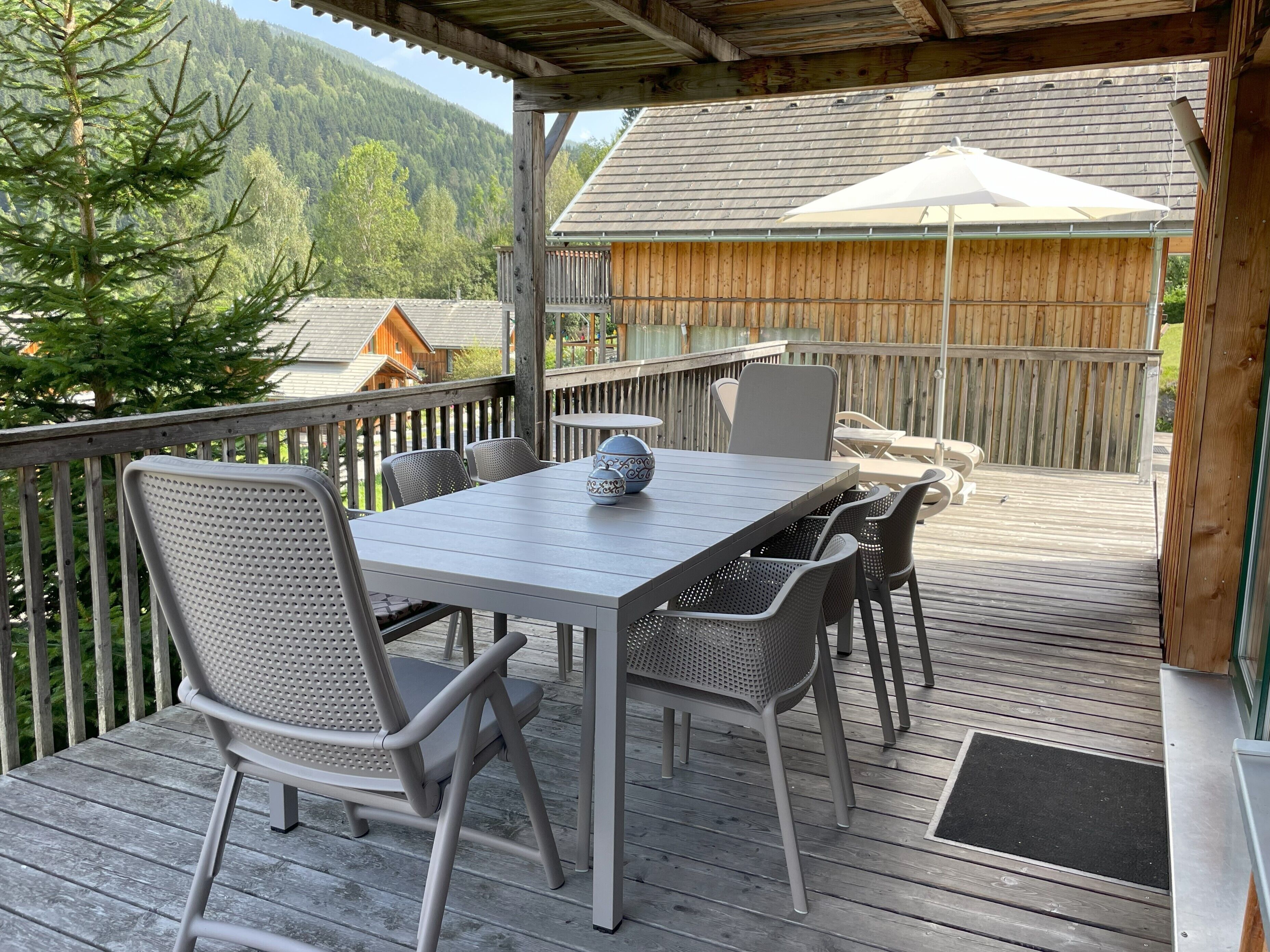 Una terraza techada al aire libre con una mesa y sillas, con vista a un área boscosa.