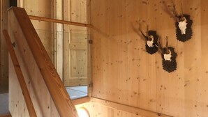 A wooden staircase with a view of a room featuring a wooden wall with mounted animal skulls.