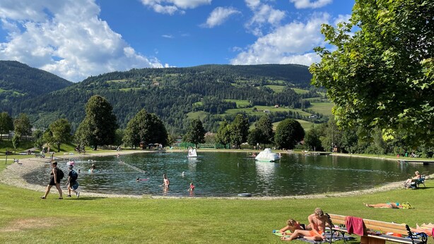 A lakeside park with a swimming area, picnic tables, and a view of green hills.