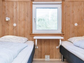 A room with wooden panel walls, two beds with white linens, a small white table, and a window with a view of greenery. - 12 Person Holiday Home in Hvide Sande (Hvide Sande)