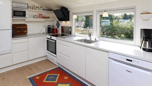 Una cocina moderna con armarios blancos, microondas integrado, estufa, fregadero y lavavajillas. Una ventana ofrece vistas a zonas verdes.
