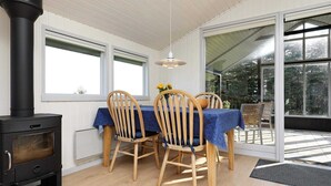 Una habitación acogedora con estufa de leña, una mesa de comedor con sillas y ventanas amplias que ofrecen vistas al exterior.