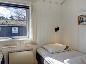 A small, single-bed room with a window, a wall-mounted light, and a shelf. - 4 Star Holiday Home in Nexo (Nexø)