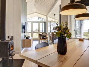 A modern interior with a wooden dining table, a vase with flowers, and a large window offering a view of the outdoors. - 4 Star Holiday Home in Nexo (Nexø)