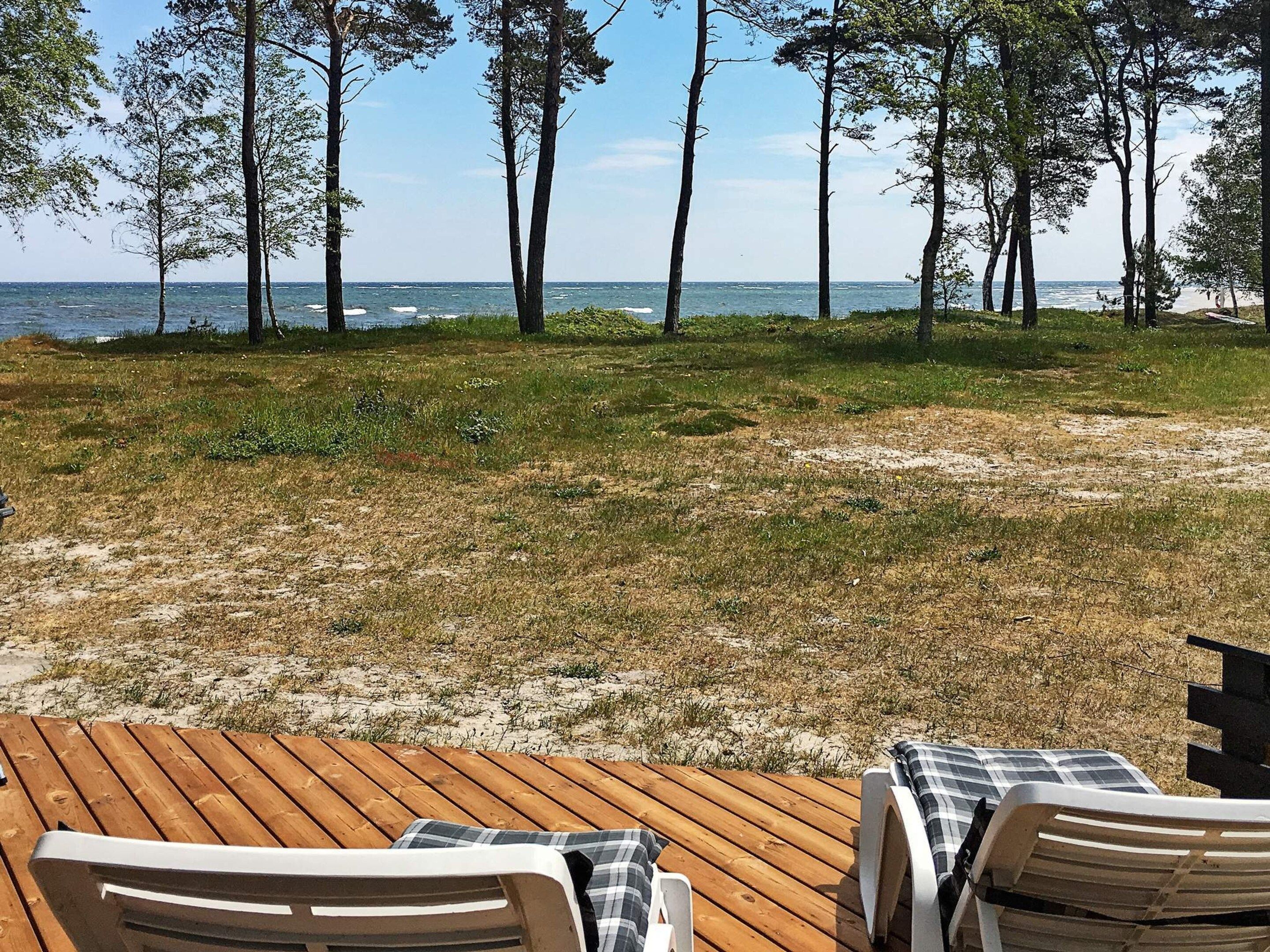 A wooden deck with two lounge chairs facing a beach with trees and the ocean in the background.
