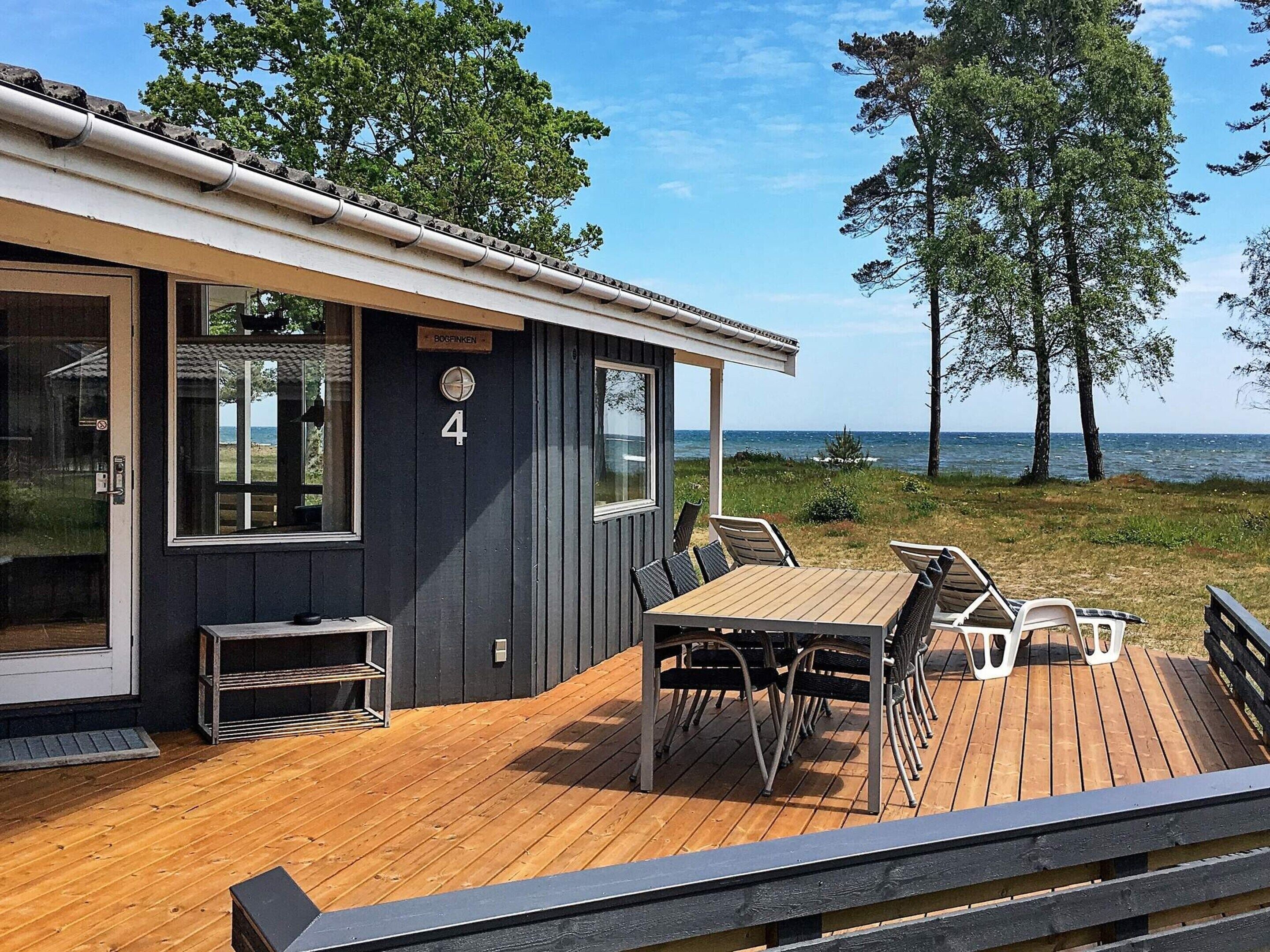 A wooden deck with a table and chairs, a small outdoor seating area, and a view of the sea.