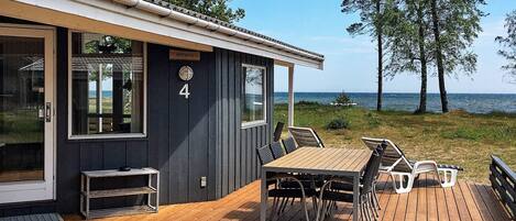 A wooden deck with a table and chairs, a small outdoor seating area, and a view of the sea.