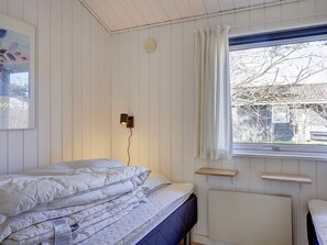Une chambre à coucher avec un lit, une lampe fixée au mur, une fenêtre avec des rideaux et un radiateur.