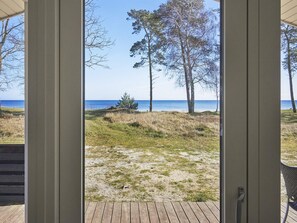 A view from a room with a wooden deck leading to a grassy area with trees and a body of water. - 4 Star Holiday Home in Nexo (Nexø)