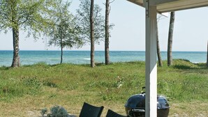 A covered outdoor seating area with a table, chairs, and a grill, overlooking a grassy area with trees and a view of the sea. - 4 Star Holiday Home in Nexo (Nexø)