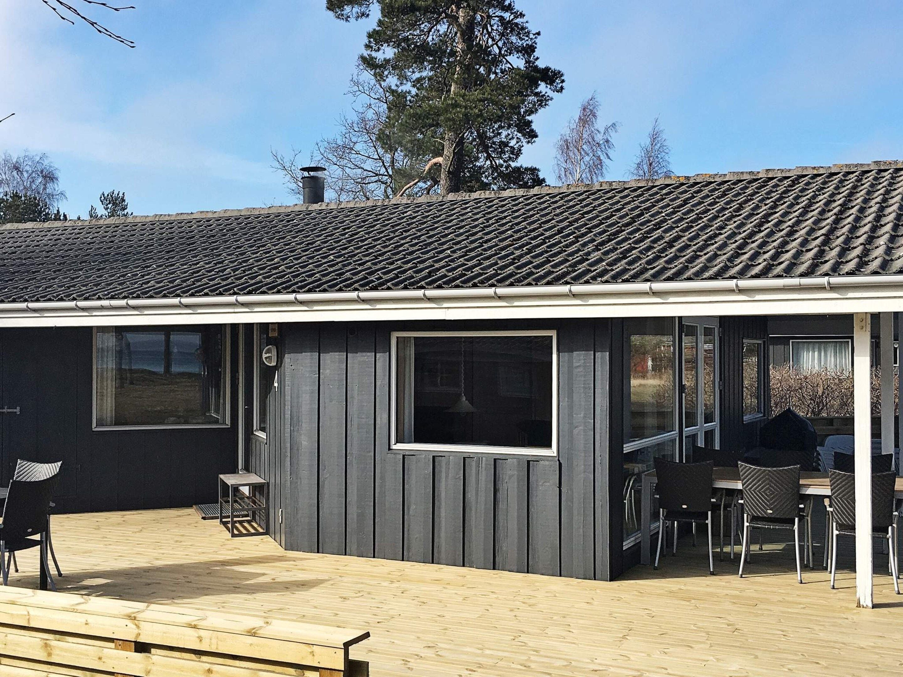 Un bâtiment à l’extérieur sombre, doté d’un toit en tuiles et d’une terrasse en bois avec des sièges pour l’extérieur.