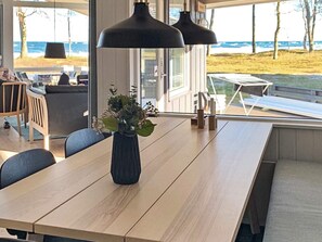 A modern dining area with a wooden table, chairs, a vase with flowers, and pendant lights. - 4 Star Holiday Home in Nexo (Nexø)
