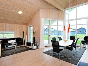 Een ruime kamer met een houten plafond, een groot raam, een zithoek met een tafel en stoelen, en een zwarte bank.