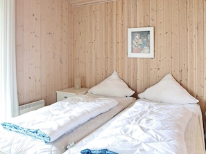 A room with two beds, wooden panel walls, a framed picture, and a bedside table with a lamp.