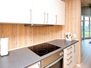 A modern kitchen with wooden cabinetry, a built-in stovetop, and a kettle on the counter.