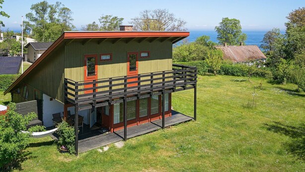A two-story house with a balcony, a wooden deck, and a view of the sea.