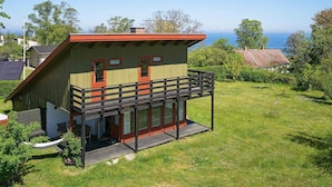 A two-story wooden house with a balcony, surrounded by a grassy yard and trees. - 8 Person Holiday Home in Allinge (Allinge)