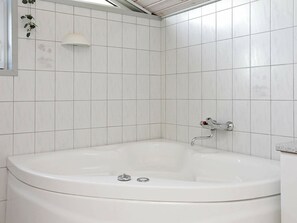 A bathroom with a white bathtub, tiled walls, and a wall-mounted light fixture. - Sprawling Holiday Home at Hvide Sande With Indoor Whirlpool (Hvide Sande)